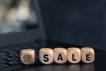 Wooden cube with the word SALE on laptop keyboard background