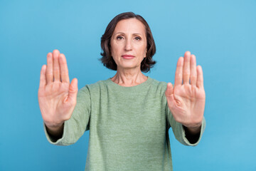 Photo of old grey hair woman show stop gesture emotion wear green jumper isolated on blue color...