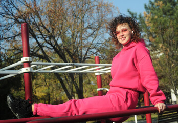Cute curly hair woman in pink sportswear makes exercises on playground