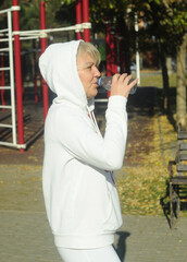 Middle age woman, 50 years,  with a headphones drinking water on the playground