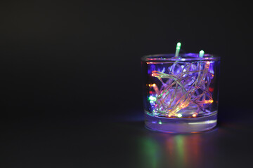 Glass with Christmas lights on black background.