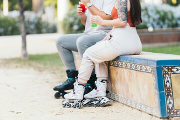 Two people wearing inline skates sitting outdoors while drinking colorful drinks