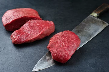 Stof per meter Rauwe, droge, oude bizon beef rump steak stuk en plakjes aangeboden als close-up op zwarte achtergrond met kopieerruimte © HLPhoto