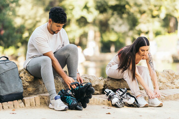 Young couple sitting on a park puting on inline skates