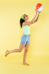 full length of happy african american woman in sunglasses playing with inflatable ball on yellow