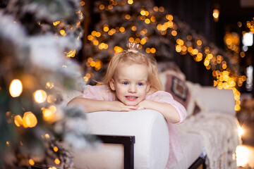 A cute charming girl smiles sincerely. The child is waiting for Christmas. Portrait of a child for the new year. Festive bokeh garland decorations. Copy space