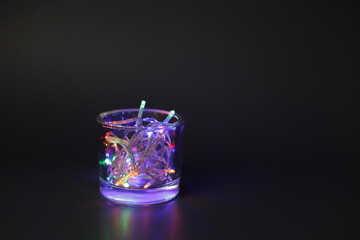 Glass with Christmas lights on black background.