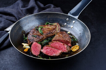 Traditional fried dry aged bison beef rump steaks with herbs and garlic served as close-up in a rustic metal skillet
