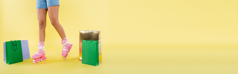 cropped view of african american woman in roller skates near shopping bags on yellow, banner