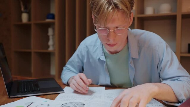 Guy searching through the dictionary book and writing in his notes.Young man studying in warm wood room. Doing homework in the evening. High quality 4k footage