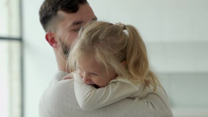 Portrait of a cute little girl in her father's arms. A father and his daughter, a baby girl, play cuddling.