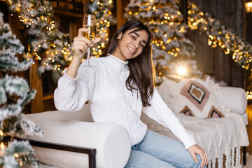 young girl raises a toast for christmas. Glass of champagne in hand. Make a wish for the new year. Positive emotions sincere smile. A woman of oriental appearance. Mix race. Christmas atmosphere mood