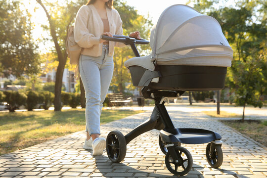 Young mother walking with her baby in stroller at park on sunny day, closeup