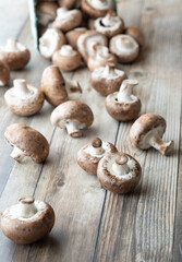 Fresh cremini mushrooms spilling out of a produce carton onto a wooden table.
