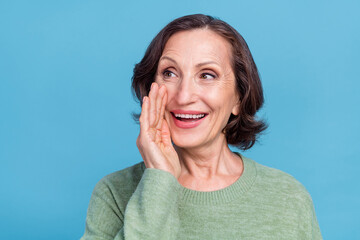 Photo of aged grey hair curious woman tell secret wear green sweater isolated on blue color background