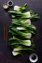 Bok choy clusters in a row with sesame seeds, soy sauce and chopsticks.