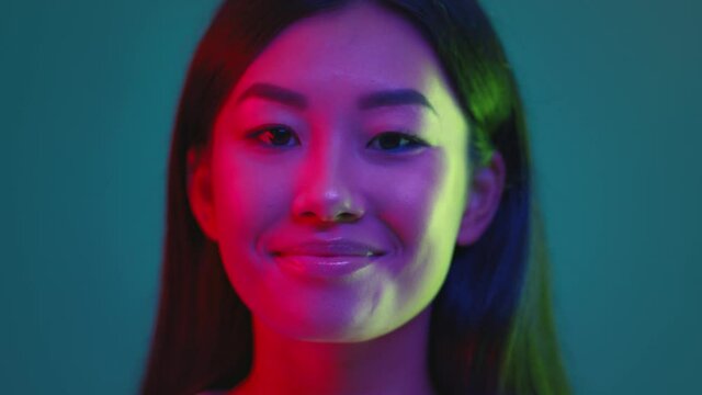 Studio portrait of young millennial korean lady turning to camera and smiling, posing in bright neon illumination
