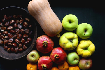 Pan with chestnuts, butternut squash and various fruit on dark background. Flat lay.