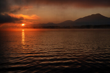 Colorful sunrise over morning lake. Reflection of orange light from the sun on water level.