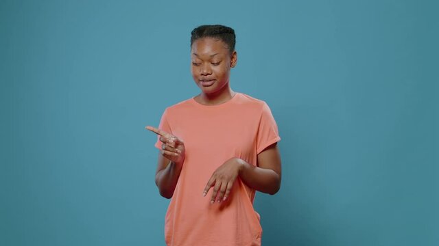 African American Woman Pointing Fingers Sideways In Studio. Young Person Indicating Left And Right Direction Doing Gesture With Hands, Advertising Sides. Positive Adult Looking Aside.