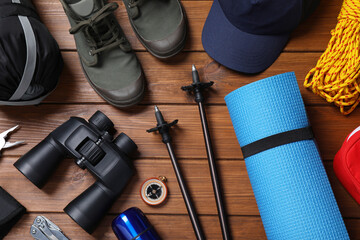 Flat lay composition with trekking poles and other hiking equipment on wooden background