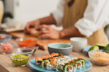 Close up making sushi rolls process. Rolls on a plate, Ingredients for sushi on a table, and master's hands on background. Sushi delivery