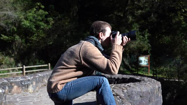 Young man taking photos on a bridge with a professional DSLR camera. 