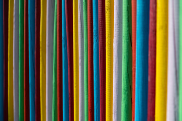 Colorful palisade fence made of wooden poles bars painted with different bright intensive colors. Yellow, green, red, blue and white alternating and forming contrasting pattern. Background lit by sun.