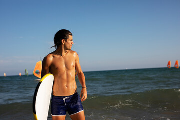 Portrait of handsome surfer with his surfboard. Young man with a surfboard on the beach.