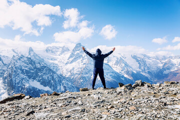 A man high in the mountains with his hands up. Sports and active tourism. Back view. Beautiful landscape.