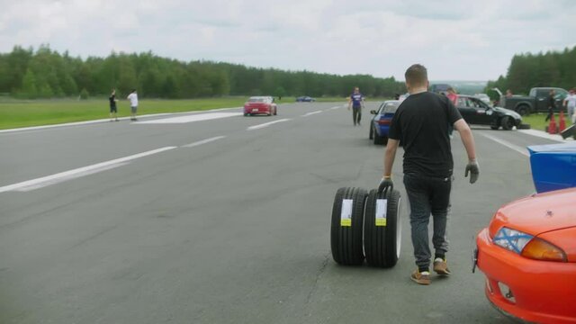 A mechanic rolls two new, freshly assembled wheels along the road, a forest and a blue sky in the background.