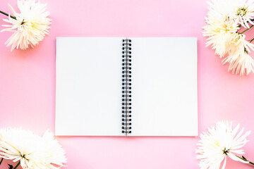Blank notepad and chrysanthemum flowers on pink background. Copy space for text. Top view, flat lay