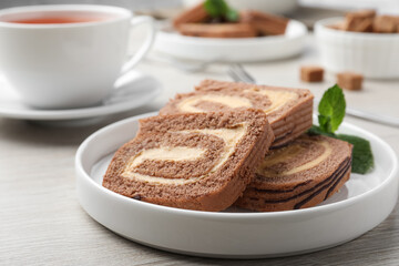 Tasty chocolate cake roll with cream on light wooden table, closeup