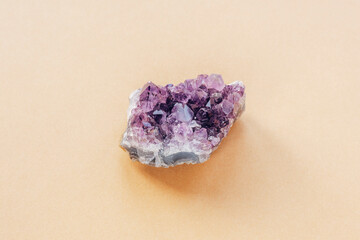 Purple amethyst crystal on a light beige background, close up. Top view