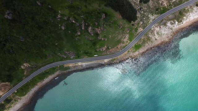 Top down drone shot. Fly over a spectacular coastal road. Picturesque view of the shoreline. Tranquil sea with  turquoise water. Some cars, motorbikes are going by this beautiful road.Con Dao,Vietnam.