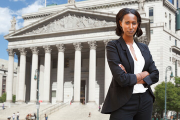 A well dressed woman with arms folded standing in front of a courthouse or municipal building. Could be a lawyer business person etc.