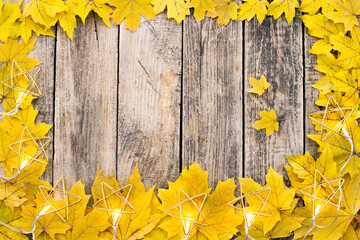 Yellow leaves on a wooden background with a garland. Top view