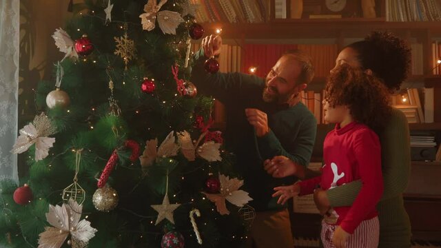 Mixed race family decorating Christmas tree together at apartment
