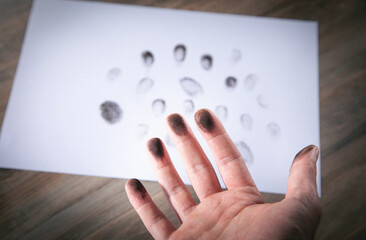 Male hand with a black print of fingers on paper.