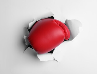 Man breaking through white paper with boxing glove, closeup