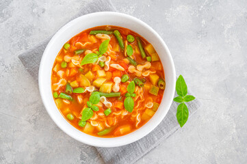 Minestrone soup of fresh vegetables and pasta in a bowl on a gray concrete background. Vegan dish. Copy space.