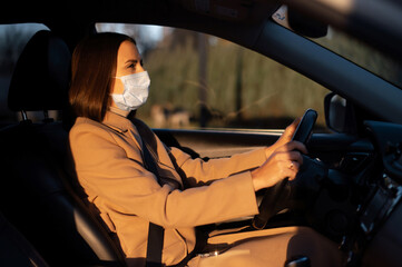 Young businesswoman in autumn coat wearing medical mask on the face is driving a car. Keep yourself in safety during pandemic