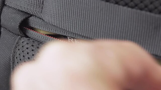 A person removes a smartphone from the pocket of a backpack with RFID protection and zips it up.