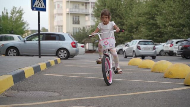 Cute girl rides a white bike down the road. Happy child rides a bike down the street. Concept of a happy childhood