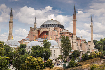 An exterior picture of Hagia Sophia museum showing beautiful colors of the building surrounding by green trees under the blue sky with white clouds.
