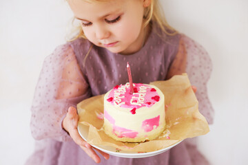 Little white Birthday girl with cake in a pink dress laughs. Preschooler. 