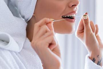 cropped view of tattooed young woman holding dental floss in bathroom