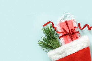 Christmas Santa hat with protective face mask and evergreen pine branches on blue background. Holiday greeting card with copy space. Top view. Medical concept.