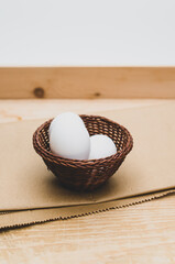 white eggs in a wicker canister on a wooden  and brown paper background with text space