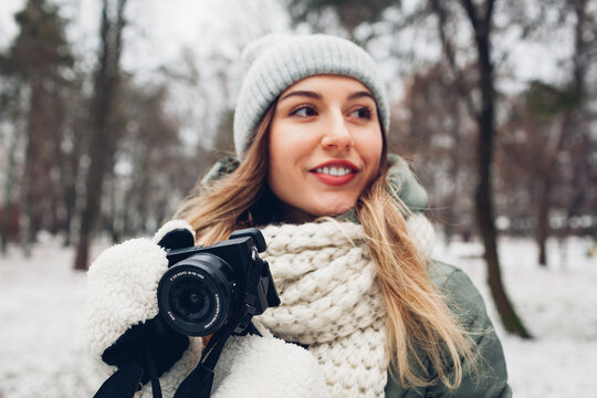Woman photographer takes pictures of snowy winter park using camera wearing warm clothes. Outdoor activities